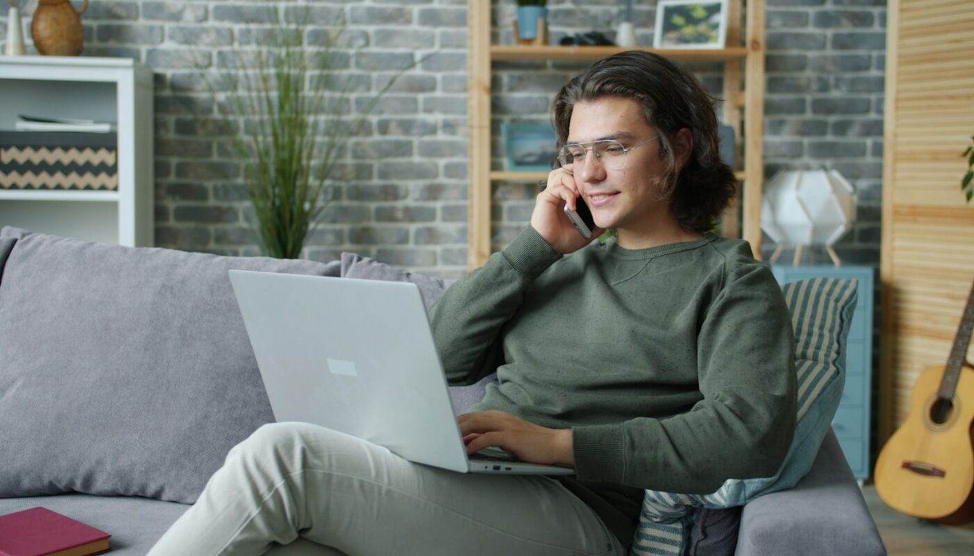 Man talking on phone while using laptop on couch