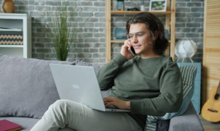 Man talking on phone while using laptop on couch